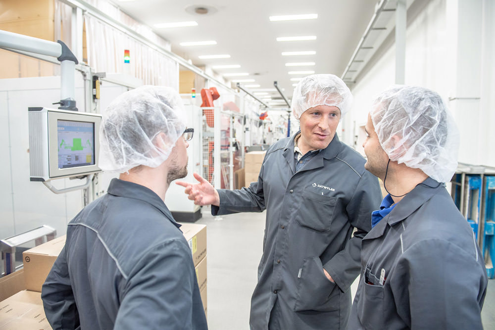 Three employees talking in front of the digital interface of a packaging facility.